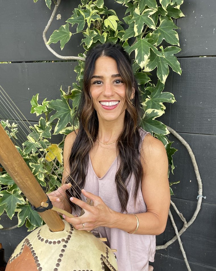 Anita smiling while playing the kamale n'goni in front of climbing ivy